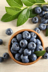 Bowl of fresh tasty blueberries with leaves on table, flat lay