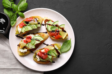 Delicious bruschettas with balsamic vinegar and toppings on black table, flat lay. Space for text