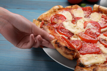 Woman taking piece of delicious Caprese pizza at blue wooden table, closeup