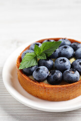 Tartlet with fresh blueberries on white wooden table, closeup. Delicious dessert