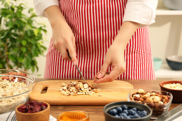 Obraz na płótnie Canvas Making granola. Woman cutting nuts at table in kitchen, closeup