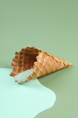 Melted ice cream and wafer cone on green background, closeup