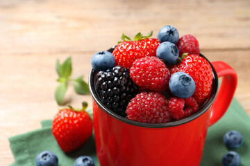 Many different fresh ripe berries in mug on wooden table, closeup. Space for text