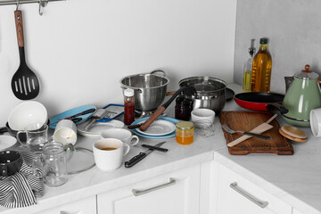 Many dirty utensils, cookware and dishware on countertop in messy kitchen