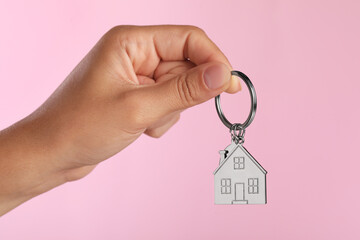Woman holding metallic keychain in shape of house on pink background, closeup