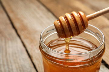 Pouring honey from dipper into jar on table, closeup. Space for text