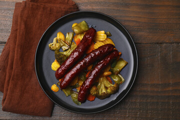 Delicious smoked sausages and baked vegetables on wooden table, top view