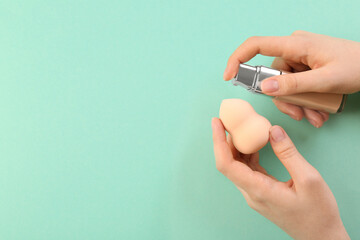 Woman adding skin foundation onto makeup sponge on mint color background, top view. Space for text