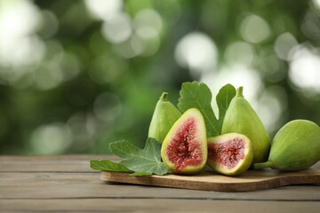 Cut and whole green figs on wooden table against blurred background, space for text