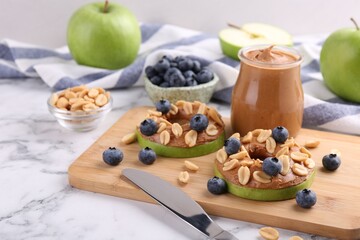 Fresh green apples with peanut butter, blueberries and nuts on white marble table