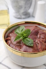 Bowl with raw chicken liver and basil on table, closeup