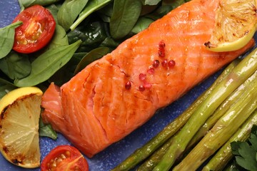 Tasty grilled salmon with tomatoes, asparagus, lemon and basil on plate, top view