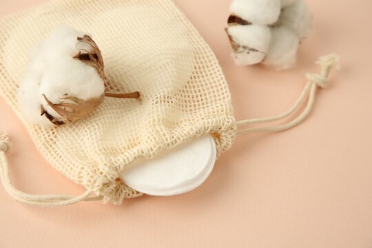 Bag with cotton pads and flowers on beige background, closeup