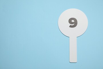 Auction paddle with number 9 on light blue background, top view. Space for text