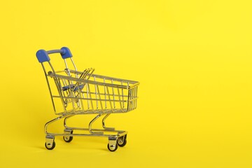 Small metal shopping cart on yellow background. Space for text