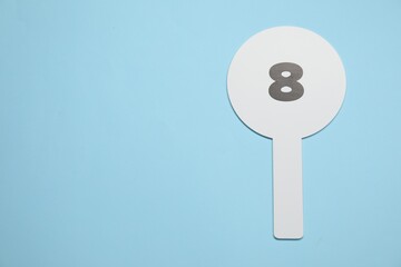 Auction paddle with number 8 on light blue background, top view. Space for text