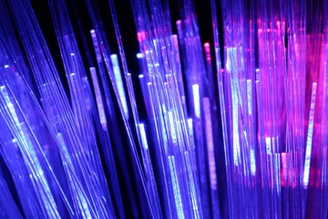 Optical fiber strands transmitting different color lights on black background, macro view