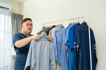 Asian young man with down syndrome and choosing clothes on closet rack. 
