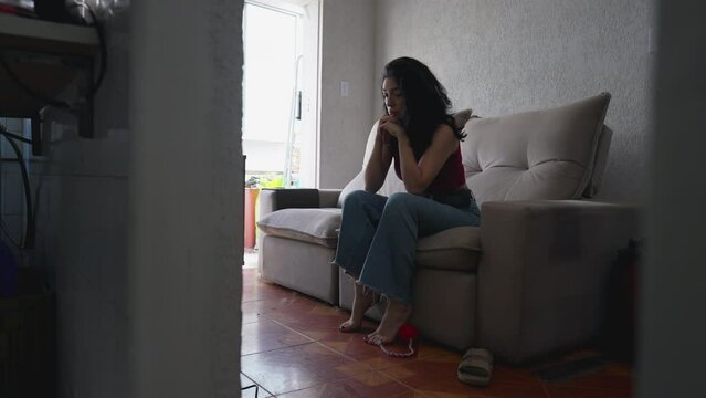 One pensive young woman feeling alone at home sitting on couch sofa inside apartment. Thoughtful female person in 30s feeling solitude