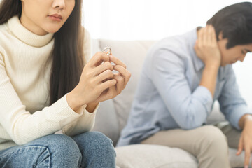 Stressed asian young couple man, woman quarrel on couch, relationship in trouble. Wife's hand holding wedding ring in disappointment and upset her husband, which may lead to divorce. Problem of family