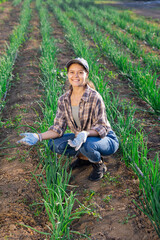 Satisfied woman owner of a farm plantation demonstrates grown green onions in the field beds