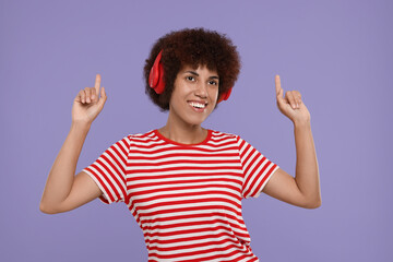 Happy young woman in headphones enjoying music on purple background