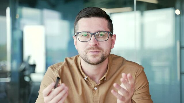 Webcam view. Close up. Confident businessman talking at a business meeting on a video call sitting in office looking at camera. Teacher or tutor speaks remotely at an online course, seminar or lecture