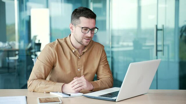 Businessman talking at a business meeting on a video call using a laptop computer while sitting at a workplace in office. A teacher or tutor speaks remotely at an online course, seminar or lecture