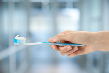 Woman holding toothbrush with toothpaste against blurred background, closeup