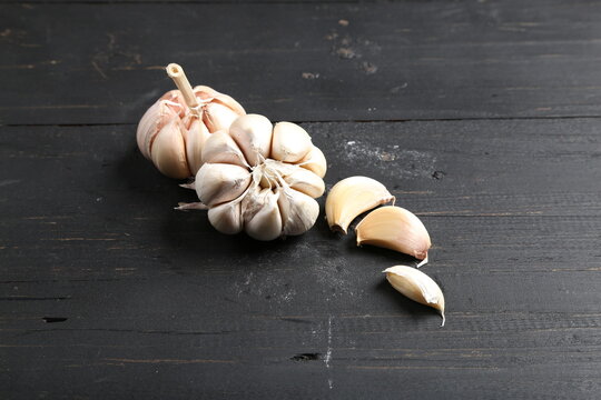 Several cloves of garlic placed on a black rustic wooden board.