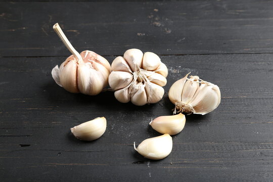 Several cloves of garlic placed on a black rustic wooden board.