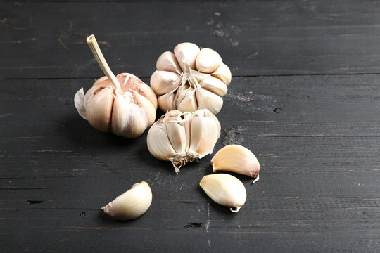 Several cloves of garlic placed on a black rustic wooden board.