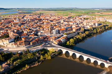 Picturesque aerial view of Tordesillas townscape on Duero river overlooking brownish tiled roofs of residential buildings and temples on spring day, Spain - obrazy, fototapety, plakaty