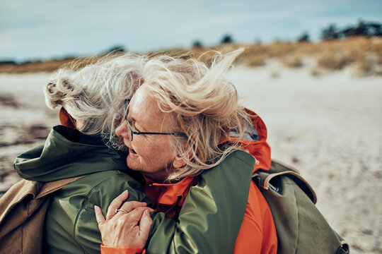 Two senior women sharing a heartfelt embrace on a breezy beach