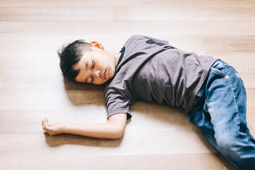 Asian little kid sleeping on the wooden floor at home. Schoolboy fainted on the floor.