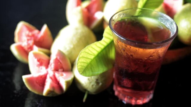 Cinematic shot of raw guava fruit cut in a stylish manner on a black wooden surface along with its extracted water in a glass alongside it. HD dolly shot. High-quality food fruit stock footage. 