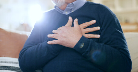 Hands, chest and heart attack with a senior man closeup on a sofa in the living room of his home...
