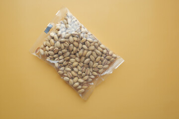 pistachios nuts in a plastic packet on orange color background 