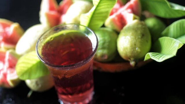 Cinematic shot of raw guava fruit cut in a stylish manner on a black wooden surface along with its extracted water in a glass alongside it. HD dolly shot. High-quality food fruit stock footage. 