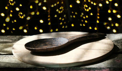 Cutting board and empty wooden spoon on the table and night background with string lights....