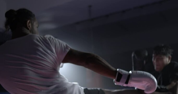 Two fighters battling each other inside boxing ring in speed-ramp slow-motion, rival lunches leg kick hitting opponent