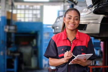 Fotobehang Happy Black female supervisor mechanic, cheerful smile, inspects repair work checklists with tablet at garage, service car maintenance, and fixing specialist occupations in auto transport industry. © tigercat_lpg
