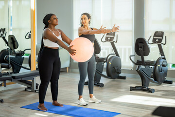 Beautiful exercise trainer enjoy helping Plus size sportive woman for yoga training by balancing body pose, doing exercises on a fitness ball. - obrazy, fototapety, plakaty