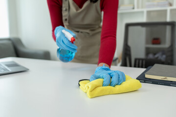 Cleaning desk surface in office with sanitizer spray, wear gloves and wipe the table with a towel, the housekeeper is cleaning the work desk for hygiene because of the Covid-19, cleaning idea.