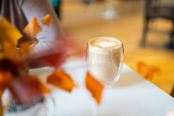 Cappuccino in glass with double walls on table in cafe background. Fall season menu. Coffee in autumn. High quality photo