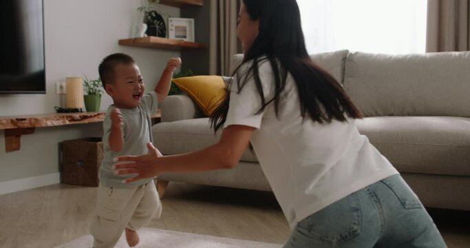 Asian kid running into mom arms. Mother lifts child up takes in arms hugs cuddle. Relationship between son and mother full of love care fun. Baby boy laughs loudly runs into mommy arms. Slow motion.