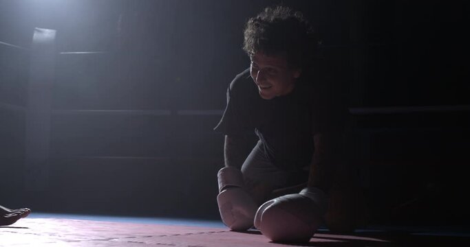 Boxer resilience theme of Man getting up from floor after takedown. Fighter wearing boxing gloves raises himself