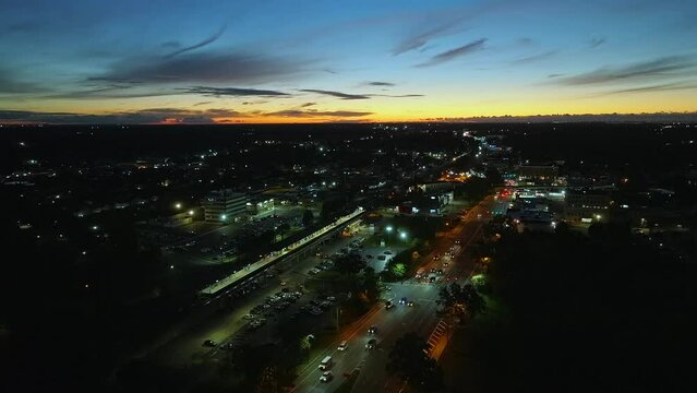 An aerial view of Sunrise Highway and a Long Island Railroad train station at sunrise. The camera dolly in, in slow-motion at 4k 59.94 fps heading towards an approaching train and vehicle traffic.