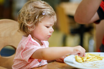 Adorable toddler girl eating healthy vegetables and unhealthy french fries potatoes. Cute happy...