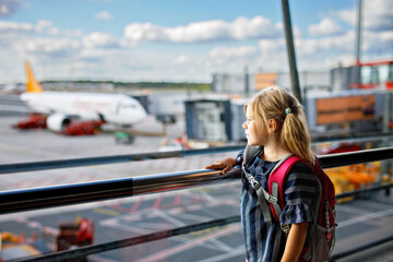 Little girl at the airport waiting for boarding at the big window. Cute kid stands at the window...